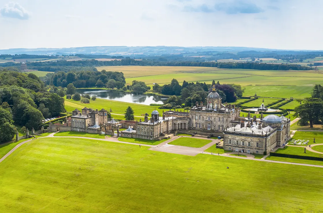 Castle Howard kuvattuna sisäpihan puolelta joidenkin satojen metrien päästä ilmasta siten, että taustalla näkyy lampi, niityt, metsää ja kukkulat